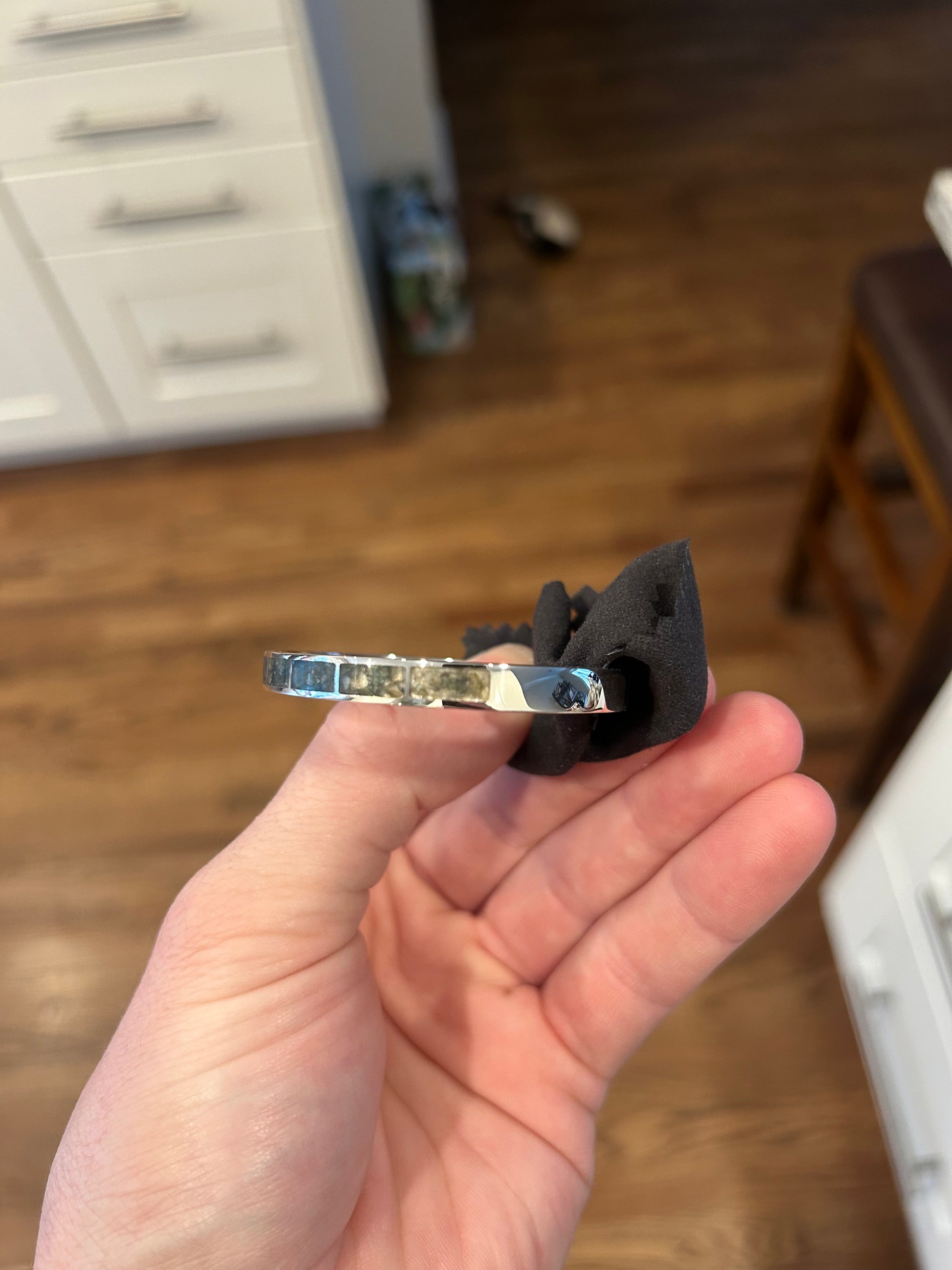 Hand holding a small metallic object with a black component against a blurred indoor background